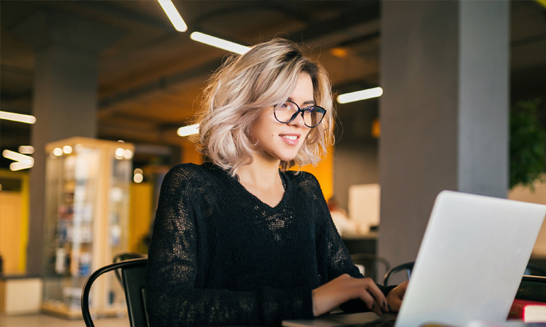 Blond girl wearing glasses using laptop smiling